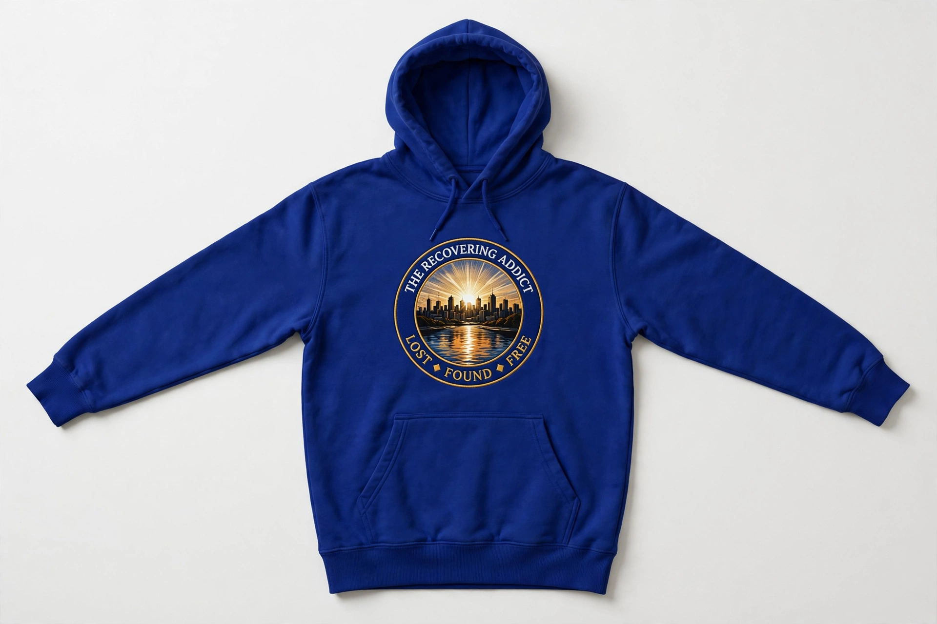 Royal-blue hoodie with The Recovering Addict circular sunrise, Minneapolis skyline, river reflection, and Lost Found Free emblem on the chest